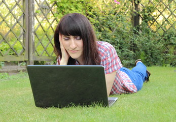 Woman with laptop lying on the grass in the sunny garden