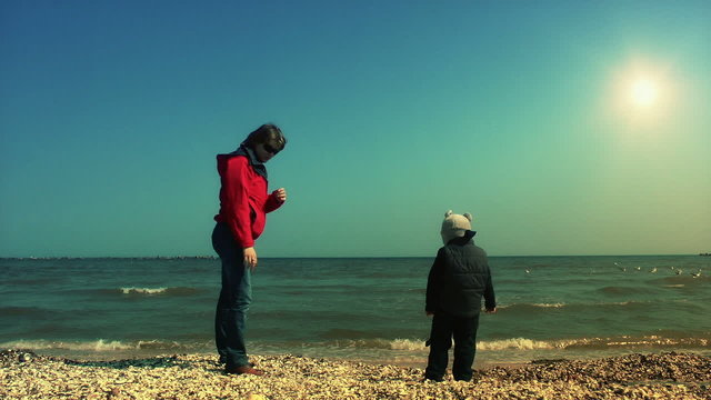 Mother teaching her son to throw sea shells