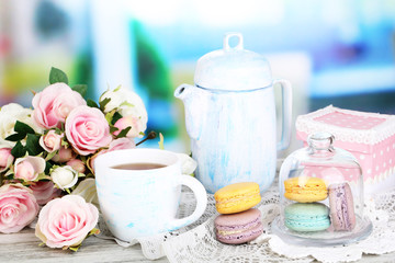 Macaroons in bowl on wooden table on room background