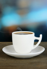 Cup of coffee on wooden table on bright background