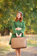Redhead girl with suitcase at tree's alley.