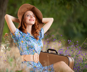 Redhead girl with suitcase sitting at autumn grass