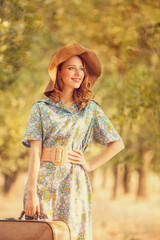 Redhead girl with suitcase at tree's alley.
