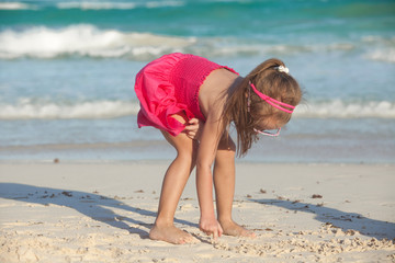 little cute girl draws on the white sand at tropical beach