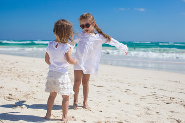 Two little sisters in white clothes have fun at tropical beach