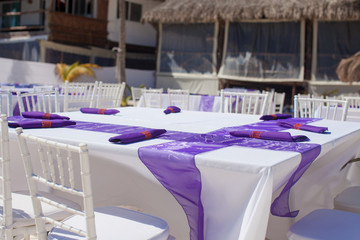 White wedding table decorated with purple bows on white sandy