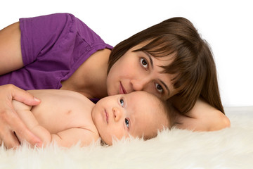 Young woman lying with her baby daughter on a sheepskin, isolate