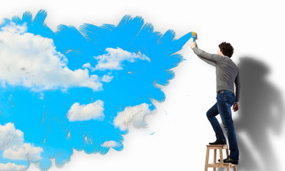 Young man drawing a cloudy blue sky