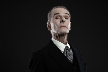 Scary count dracula in black suit. Pale head. Studio shot agains