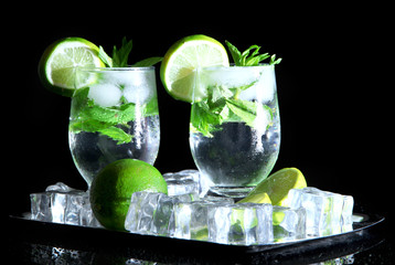Glasses of cocktail with ice on metal tray on black background