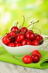 Cherry berries in bowl on wooden table on bright background
