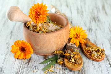 Fresh and dried calendula flowers in mortar on wooden