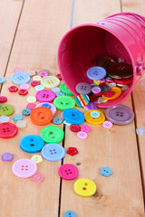 Colorful buttons strewn from bucket on wooden background