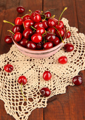 Ripe red cherry berries in bowl on wooden table close-up