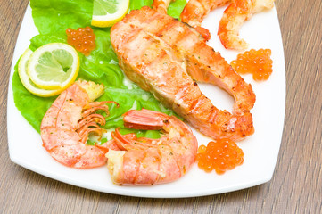 a piece of broiled fish, shrimp and red caviar on white plate cl
