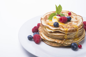 Pancakes with berries and honey on white plate