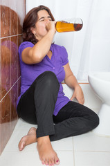 Latin woman lying drunk in the bathroom and drinking