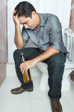 Drunk man with a headache sitting on the toilet