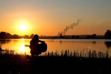 silhouette of a girl at sunrise playing the guitar by the river