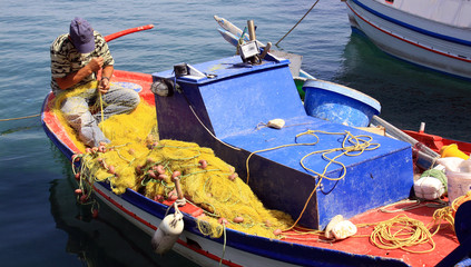 Fototapeta na wymiar Un pêcheur reprisant son filet
