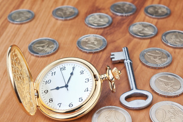 Vintage pocket watch and a key against the euro coins. Close-up.