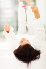 Fototapeta premium excited woman lying on bed looking at pregnancy test