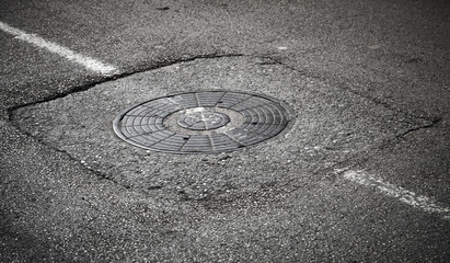 Fototapeta na wymiar Sewer manhole cover on asphalt road with white road marking
