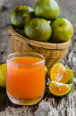 a glass of orange juice and basket on wooden background.