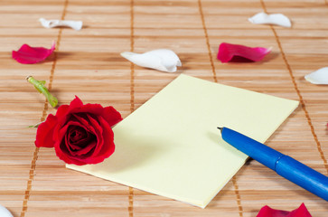 Pen and empty note on a wooden background with a rose and petals