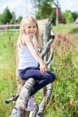 Naklejka na ściany i meble Beautiful girl with blond hair sitting on log in summer field