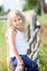 Happy disheveled blond hair girl sitting on village fence