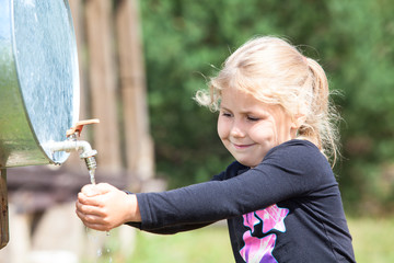 Fototapeta premium Small Caucasian child washing hand in water dispenser outdoor