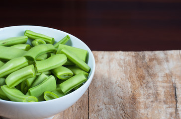 Raw green beans in a bowl, on a wooden table