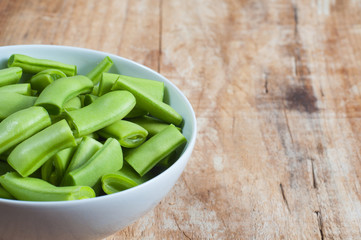 Raw green beans in a bowl, on a wooden table
