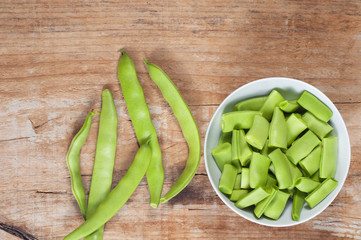 Raw green beans in a bowl, on a wooden table