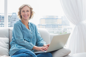 Content blonde woman sitting on her couch using laptop