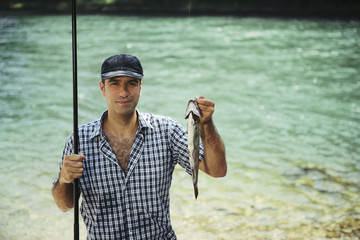 man fishing on river and showing fish to the camera