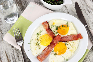 Scrambled eggs and bacon on plate on napkin on wooden table