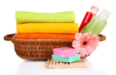 Colorful towels, cosmetics bottles and soap in basket, isolated