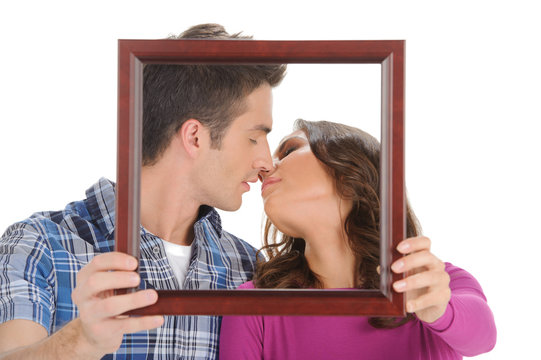 Kissing in a picture frame. Beautiful young couple holding a pic