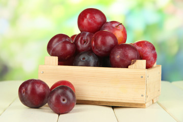 Naklejka na ściany i meble Ripe plums in wooden box on wooden table on natural background