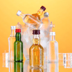 Minibar bottles in bucket with ice cubes,  on color background