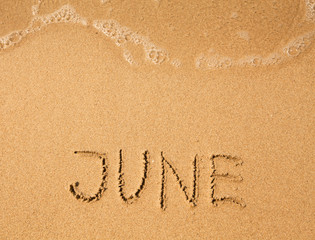 June - written in sand on beach texture (soft wave of the sea)