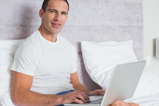 Cheerful man using laptop on bed