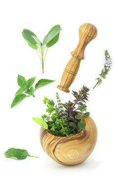 Fresh herbs falling into a wooden mortar
