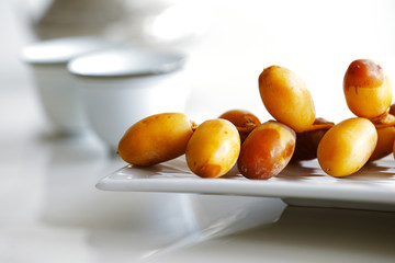 Arabic dates on a white plate with Arabic coffee cups