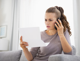 Concerned young woman holding letter and talking mobile phone