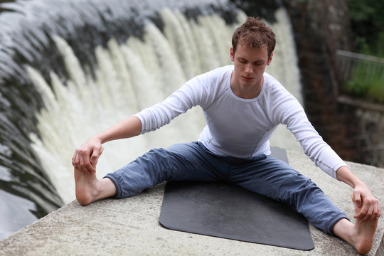 young fit man practicing stretching over waterfall - outdoor