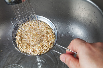 Man holding small collander rins raw quinoa seeds