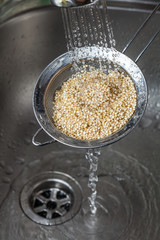 Man holding small collander rins raw quinoa seeds